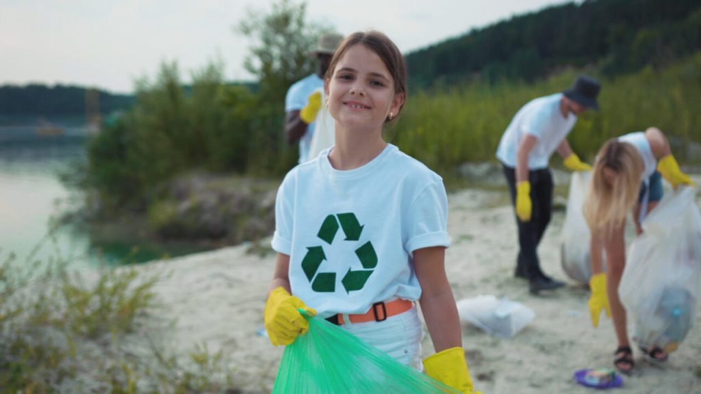 Adorable kid cleaning nature landscape from trash with environmental activists. Portrait of cute little girl volunteer smiling cleaning the beach. Save ecology.
